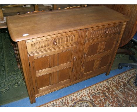 An Ercol Oak Dresser Base, having rounded corner, rectangular top with rear recessed groove, two carved front frieze drawers 
