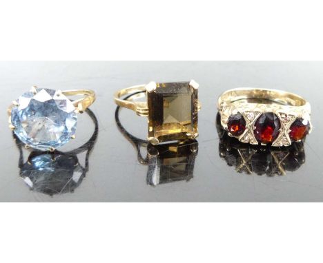 A 9ct gold blue topaz set dress ring; together with a 9ct gold smoky quartz dress ring; and a 9ct gold garnet three-stone rin