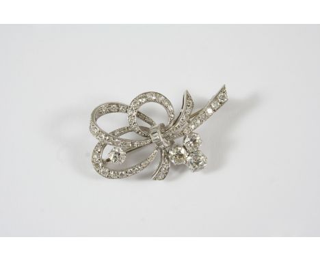 A DIAMOND BROOCH of scrolling bow design, set with four circular-cut diamonds and overall with graduated baguette-cut and cir