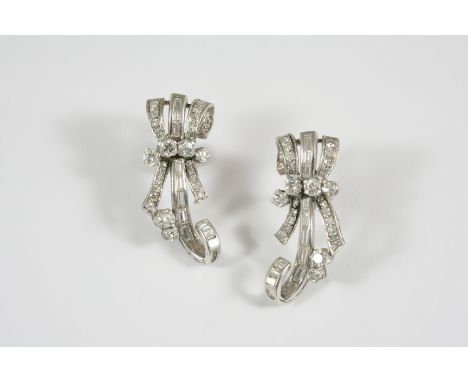 A PAIR OF DIAMOND EARRINGS each earring of scrolling bow design and set overall with baguette-cut and circular-cut diamonds, 