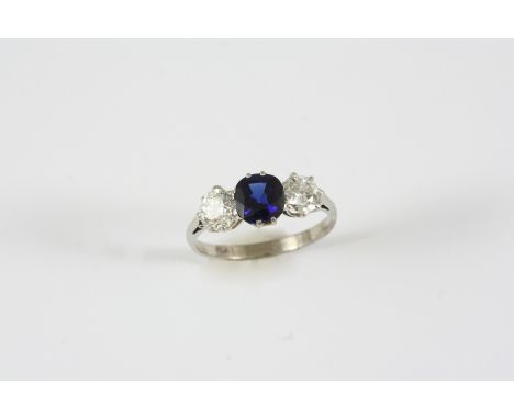 A SAPPHIRE AND DIAMOND THREE STONE RING the cushion-shaped sapphire is set with two brilliant-cut diamonds, in platinum. Size