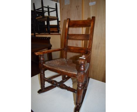 A childs oak framed rocking chair with woven fibre seat and ladder style back