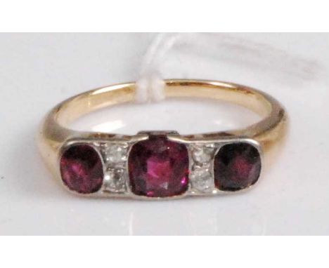 A yellow metal, ruby and diamond ring, arranged as three old cut rubies in a line setting, the centre stone weighing approx 0