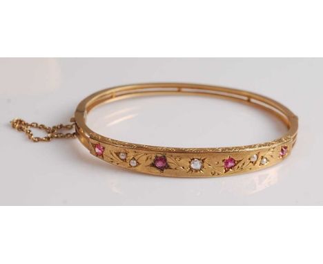 A late Victorian yellow metal, ruby, diamond and seed pearl oval hinged bangle, featuring an engraved central panel set with 