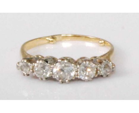 A yellow metal diamond five-stone ring, the graduated claw set round cut diamonds in a line setting, the largest centre stone