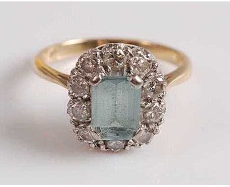 A yellow and white metal, aquamarine and diamond rectangular cluster ring, featuring an emerald cut aquamarine within a borde