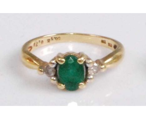 An 18ct gold, emerald and diamond dress ring, the four claw set oval cut emerald weighing approx 0.7 carats, flanked to eithe