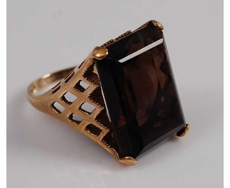 A 9ct yellow gold smoky quartz dress ring featuring a rectangular cut smoky quartz in a four-claw setting with pierced should