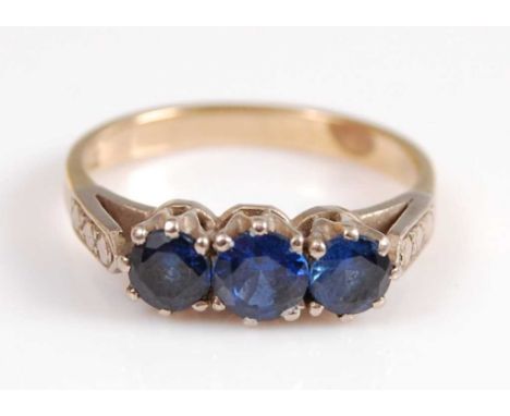 A yellow and white metal sapphire three stone ring, featuring three graduated round faceted sapphires in claw settings, with 