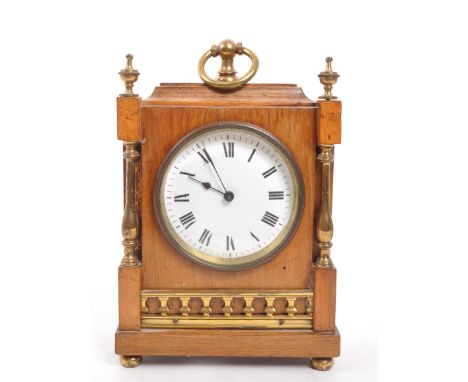 An Edwardian walnut mantel clock with brass columns to either side and brass finials to the front corners. Having brass swing