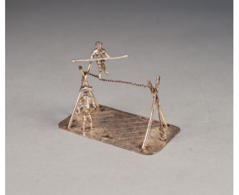 CONTINENTAL SILVER COLOURED METAL MINIATURE GROUP, of a man playing a trumpet whilst a man walks on a tight rope, on oblong b