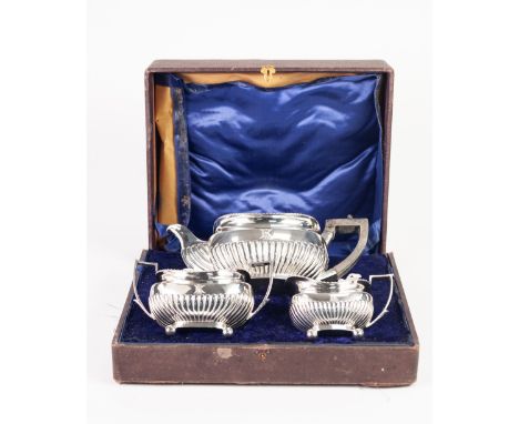 A LATE VICTORIAN CASED THREE PIECE SILVER TEA SERVICE of oval form with demi gadroon bodies, each on four ball feet, THE TEAP