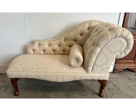 A small button back chaise lounge, upholstered in a cream floral pattern 