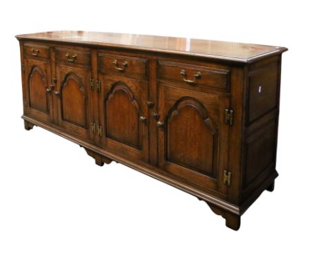A reproduction large oak sideboard. The four drawers over four panelled cupboard doors, all with brass swan-neck handles, rai
