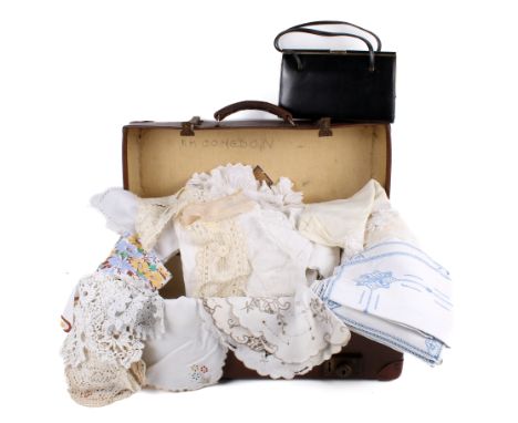 An assortment of fabric contained within a vintage brown leather suitcase. Including a crochet blanket, doilies, a black leat