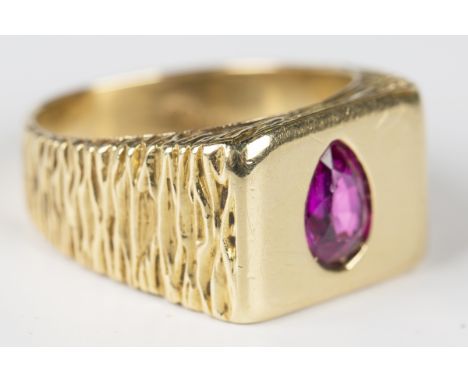 An 18ct gold and ruby rectangular signet style ring, mounted with a pear shaped ruby between bark textured shoulders, detaile