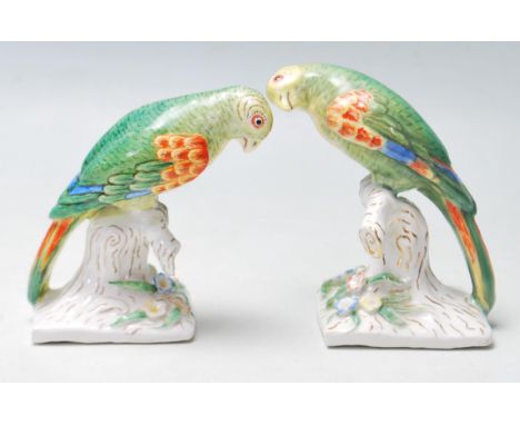 A pair of early 20th century German Continental ceramic green parrot figurines set atop a naturalistic base with polychrome d