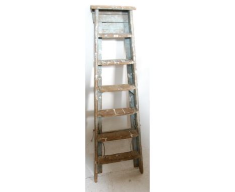 A vintage mid century Industrial folding wooden ladder having six steps and an “A-frame” setup. Complete with metal hinges at