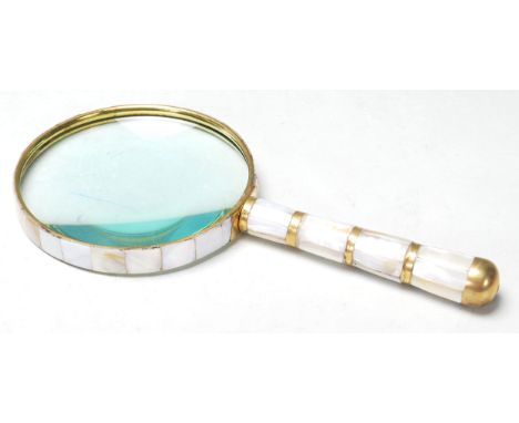 A large brass hand held magnifying glass set with faux mother of pearl along the mop handle and surrounding the lense. Measur