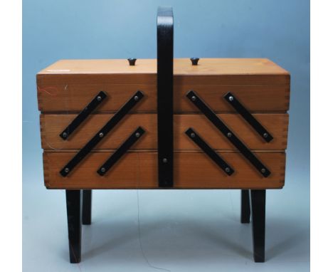 A vintage 1970’s metamorphic sewing box having arched black handle, black wooden hinges and angular legs. Measures 46 cm tall