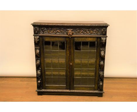 A LATE 19TH CENTURY BELGIAN OAK BOOKCASE, the carved mask-head frieze drawer above a pair of leaded light glazed doors, flank