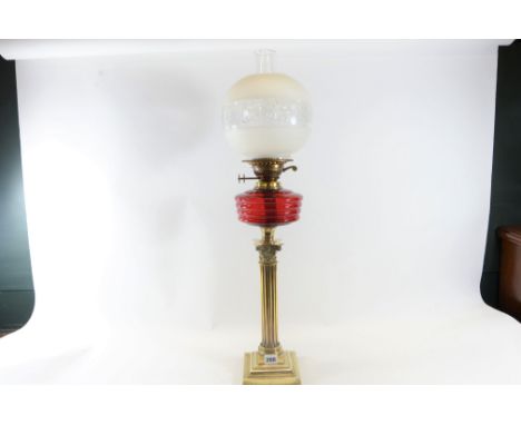 AN EDWARDIAN STYLE BRASS CORINTHIAN COLUMN TABLE OIL LAMP with ruby glass fount and duplex burner, 18 ins high, with chimney 