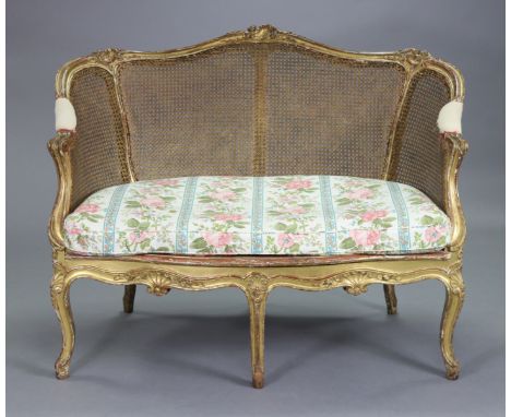 A 19th century French carved giltwood frame small sofa with rounded cane back, loose cushion seat &amp; on six cabriole legs,