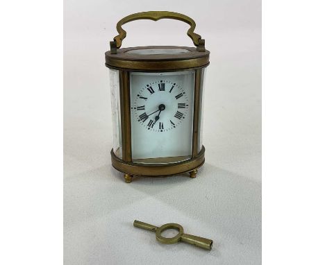 A circa 1900 French oval brass carriage clock with Roman numerals to the white enamel dial, with key, height when handle fold