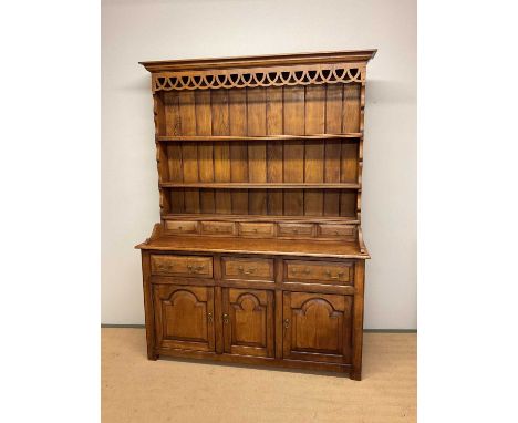 An oak dresser, the upper section having a panelled back and a three shelf plate rack above a base of three drawers above thr