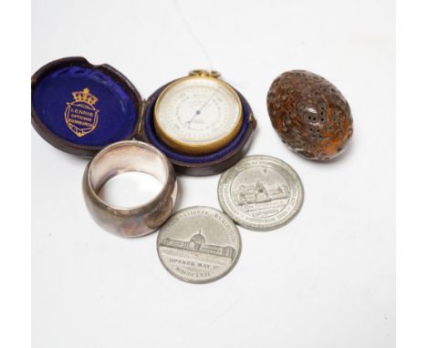 A Lennie brass pocket barometer, a carved coquilla nut, a silver plated napkin ring and two exhibition medallions