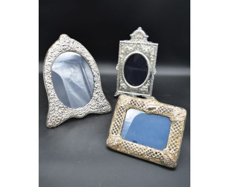 An arched silver floral embossed easel mirror and two other silver embossed mirrors each bearing English hallmarks. H.33cm W.