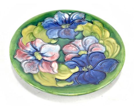 MOORCROFT; a circular plate decorated in the 'Clematis' pattern on a green ground, with original label and green signature to