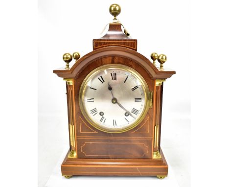 An Edwardian inlaid mahogany and boxwood strung mantel clock, the silvered dial set with Roman numerals and raised on bun fee