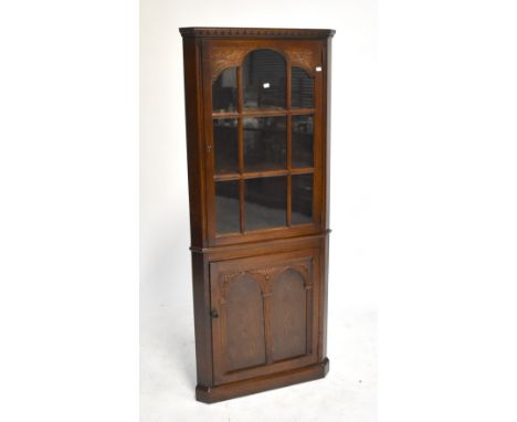 A reproduction oak corner cabinet with glazed door enclosing two shelves above single cupboard door enclosing single shelf, 1