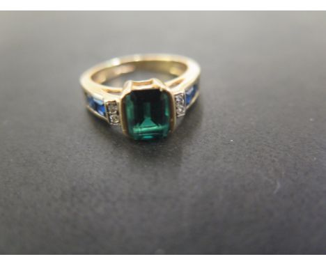 A diamond, sapphire and synthetic emerald dress ring - The rectangular synthetic emerald to the brilliant-cut diamond and squ