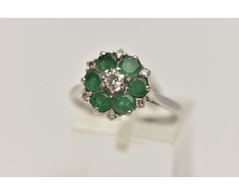 A WHITE METAL EMERALD AND DIAMOND CLUSTER RING, circular cluster, set with a central raised round brilliant cut diamond, esti