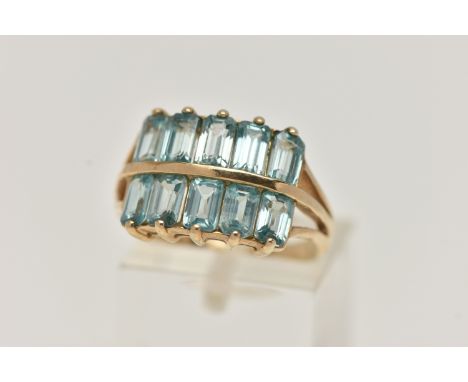 A 9CT GOLD TOPAZ DRESS RING, designed with two rows of rectangular cut light blue topaz, trifurcated shoulders, leading onto 