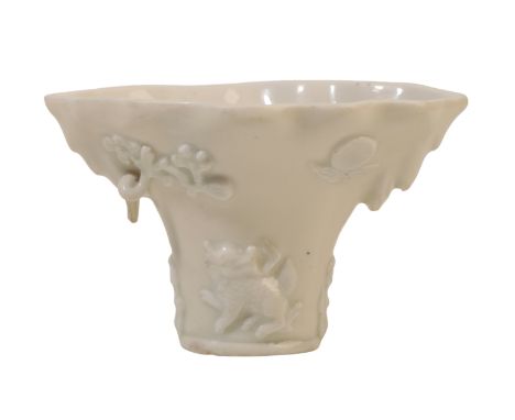 A CHINESE DEHUA "BLANC DE CHINE" LIBATION CUP imitating a rhinoceros horn vessel carved with dragons, mythical beasts and scr