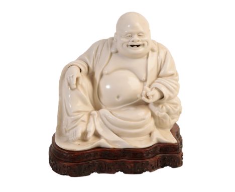 A CHINESE DEHUA "BLANC DE CHINE" BUDAI, the smiling figure reclining in loose robes holding a fruit in his left hand, probabl