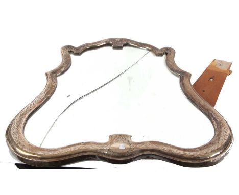 A continental dressing table mirror of escutcheon form, the metal frame engraved with a Celtic design, the arched top decorat