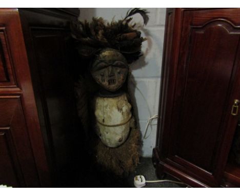 An African tribal figure of a chief with applied feather headdress, raffia cloak and straw detail, standing 62cm high  