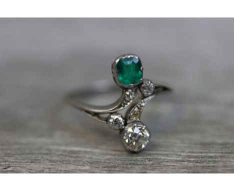 Early 20th century emerald and diamond platinum crossover ring, the cushion cut emerald measuring approximately 4.5mm x 4.0mm