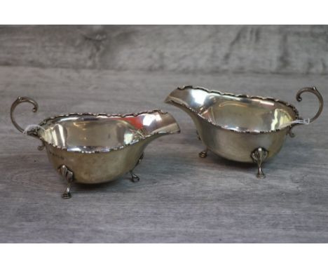 George V pair of silver sauce boats raised on three hoof feet with shell shoulders, scroll handle and Chippendale border, mak