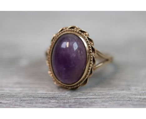 Amethyst 9ct yellow gold ring, the oval cabochon cut amethyst with rub over setting, rope twist border and barley twist surro