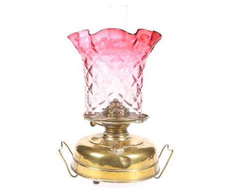 AN EARLY 20TH CENTURY BRASS OIL LAMP, with moulded cranberry tinted glass shade, the circular base with twin handles. 42cm to