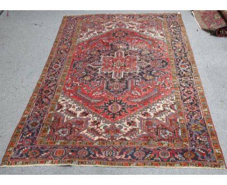 A PERSIAN HERIZ RUG,&nbsp;the raspberry lozenge field with central medallion, enclosed within a blue border. 337cm by 237cmTh