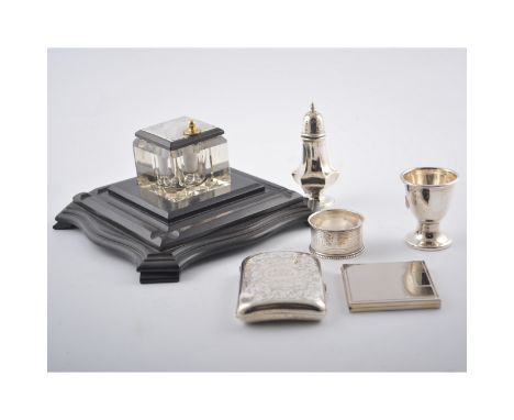 An ebonised ink stand with glass inkwell having a hallmarked silver cover, silver cigarette case, napkin ring, eggcup and sma