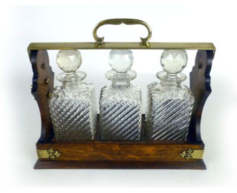 An early 20th century tantalus retailed by Mappin & Webb the oak case with brass mounts containing three pressed and cut glas