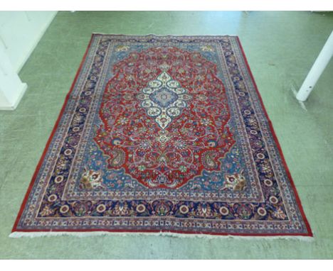 A hand woven Persian rug, the multi lined border enclosing a red ground field with a white central medallion, 367 cm x 271 cm