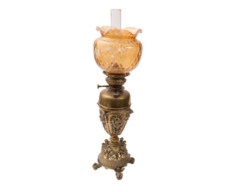 A Victorian gilt metal table oil lamp, late 19th Century; the glass flue within an amber/russet glass shade with flared rim; 